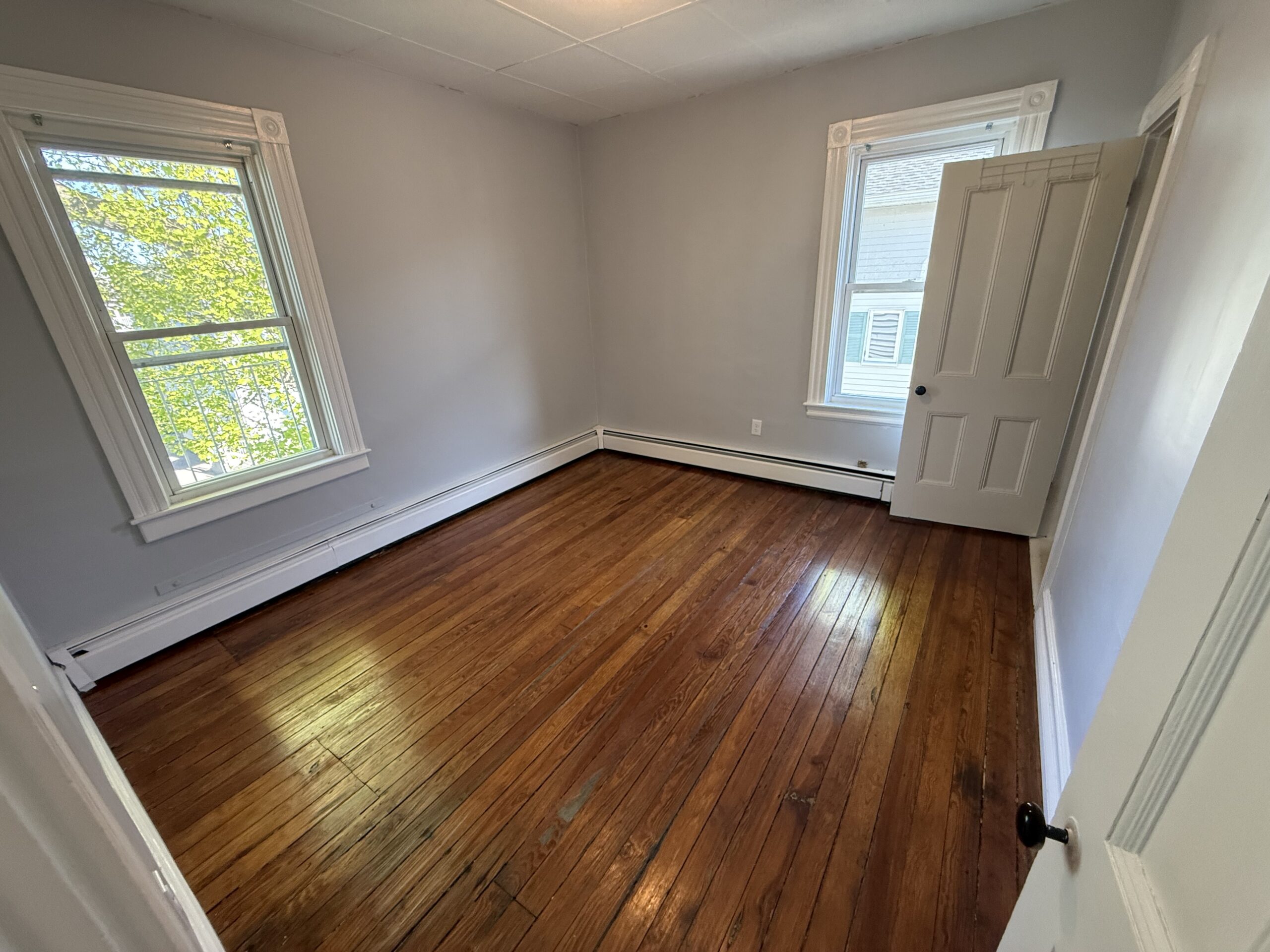 Bedroom with two windows, hardwood floor, closet, and side-yard view