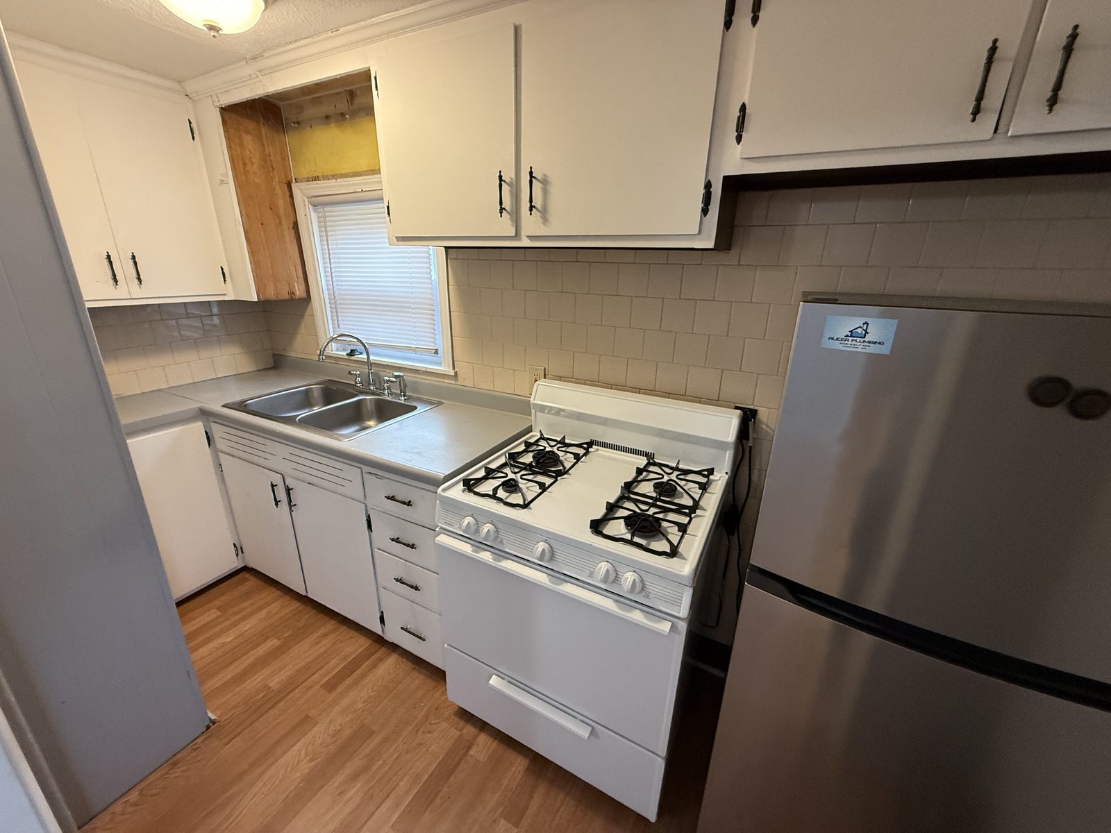 Kitchen in apartment 1N at 795 North Underwood Street Fall River MA with white cabinets, white tile backsplash, gas stove, stainless refrigerator, and double sink