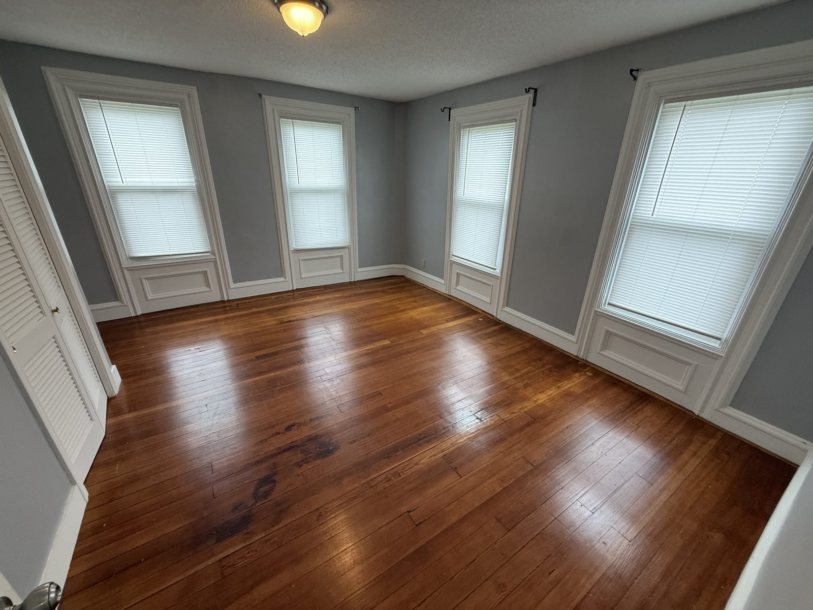 Master bedroom in apartment 1N at 795 North Underwood Street Fall River MA with four tall windows, original window trim, and hardwood floors